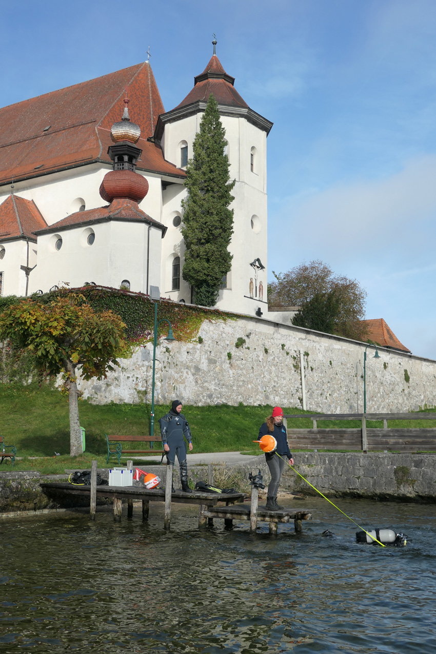 Die Forschungstaucher des Kuratoriums Pfahlbauten im Traunsee, im Hintergrund die Klosterkirche  von Traunkirchen