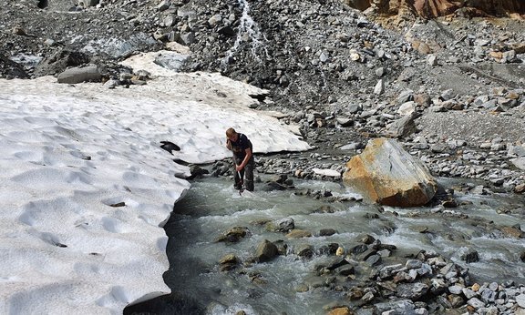 Person steht in einem Bergbach am Ende einer Gletscherzunge