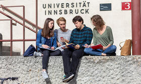Studierende sitzen auf einer Mauer