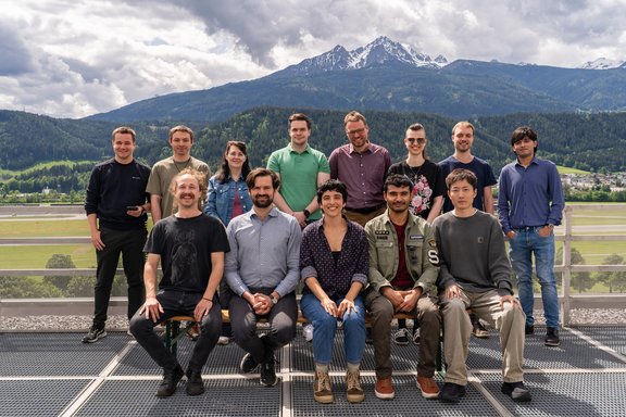 Group picture on a roof with mountains and a cloudy sky in the background.