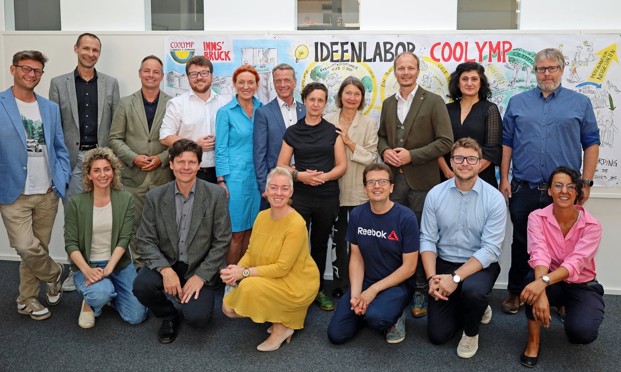 Zahlreiche Menschen stehen vor einer Plakatwand und blicken in die Kamera