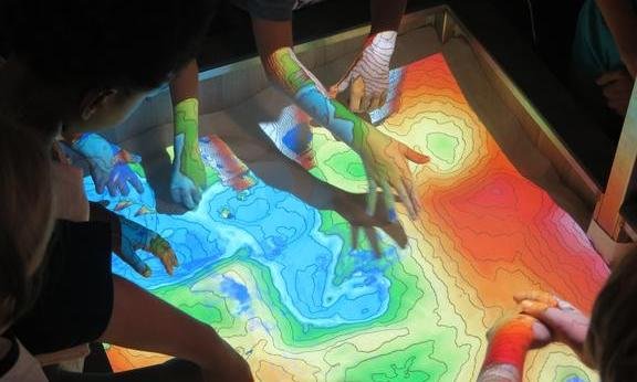 Kinder greifen in eine bunte Sandbox.