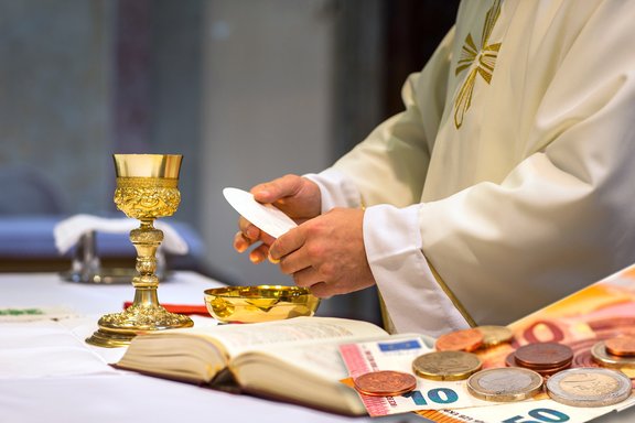 The picture shows a celebration of the Eucharistic, banknotes, and coins.