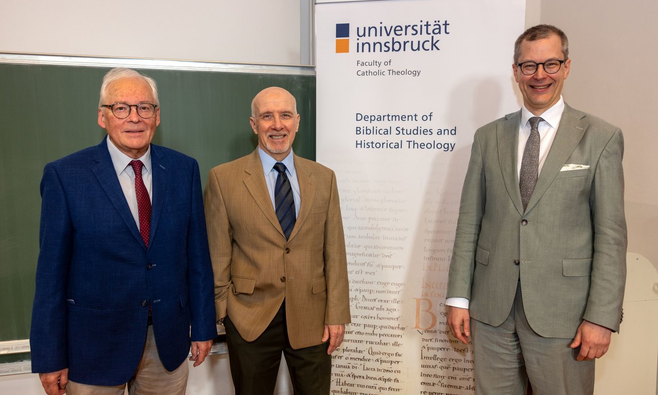 Drei Personen stehen vor einem Roll-up mit dem Logo der Universität