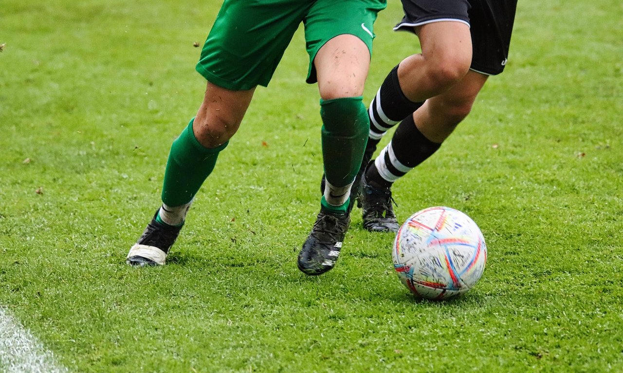 Die Beine von zwei Fussballspielerin in grünen und schwarzen Trikots, die um einen Ball kämpfen.