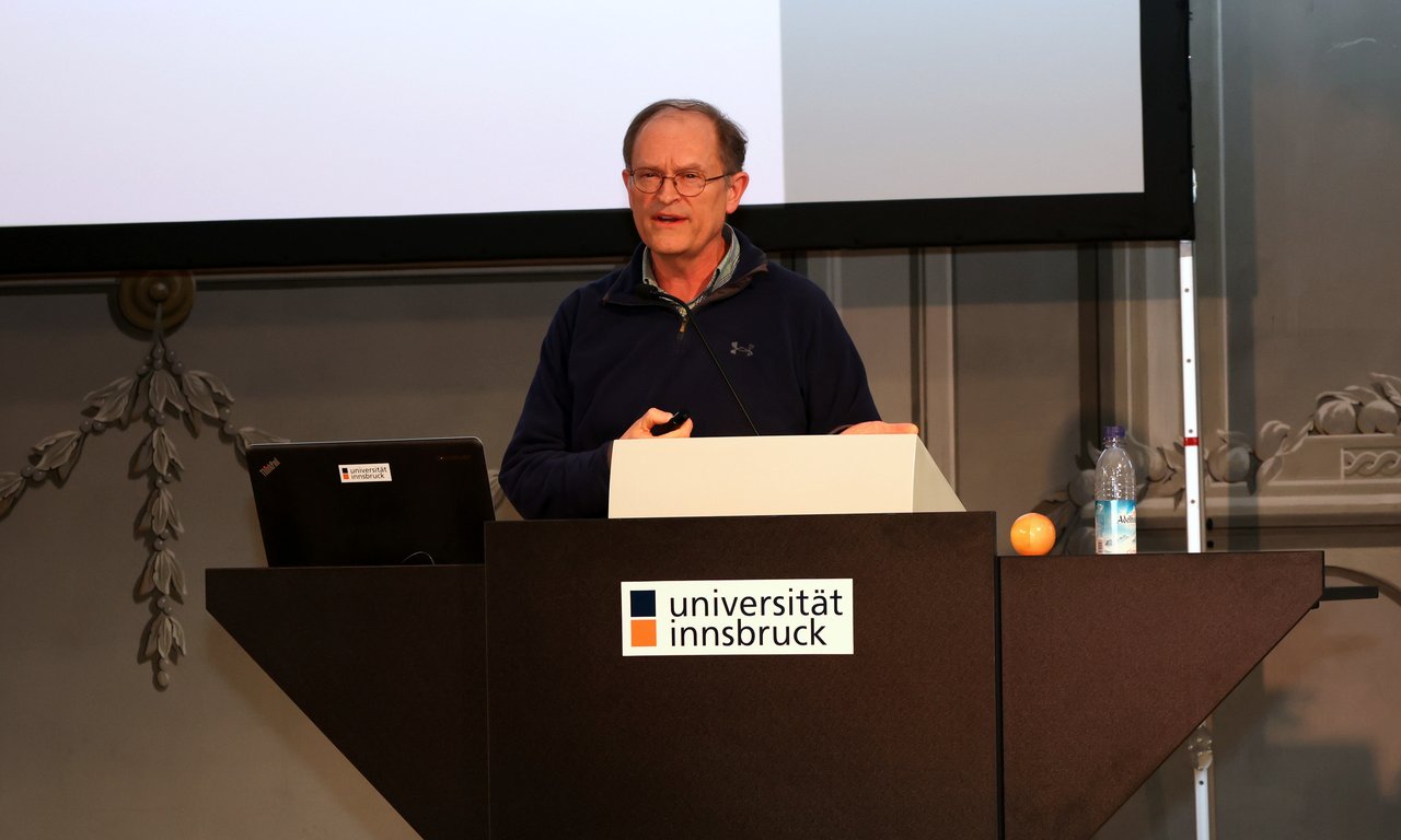 Eine Person steht am Rednerpult mit dem Logo der Universität Innsbruck