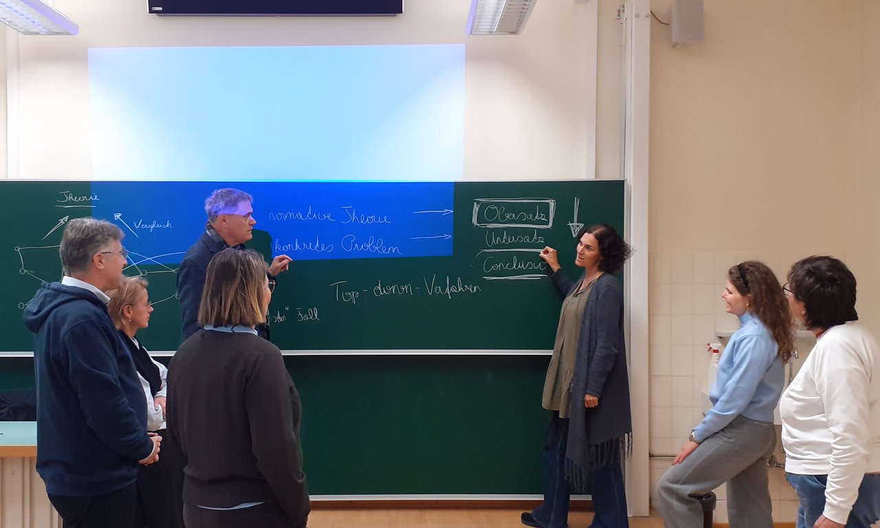 Lehrende und Lernende stehen vor einer Tafel mit Notizen