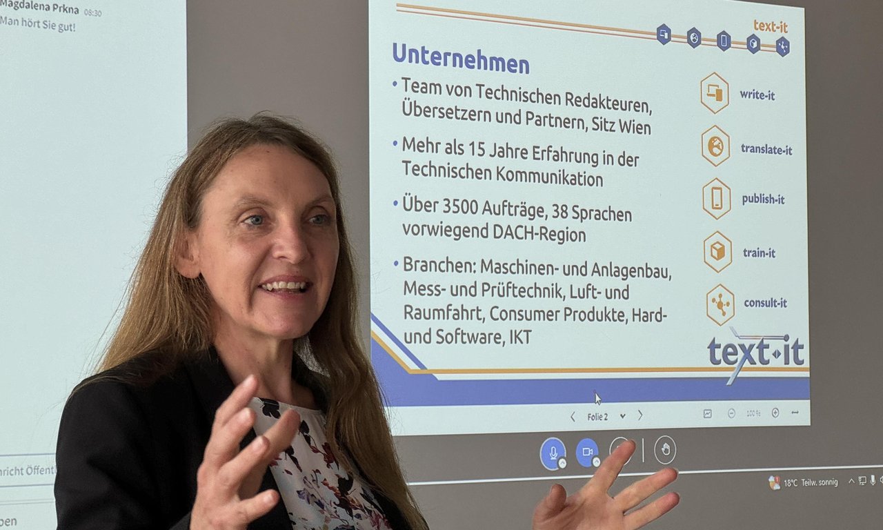 Eine Frau in Nahaufnahme bei einem Vortrag, im Hintergrund ist auf einer Leinwand eine Folie mit einer Unternehmensvorstellung zu sehen.