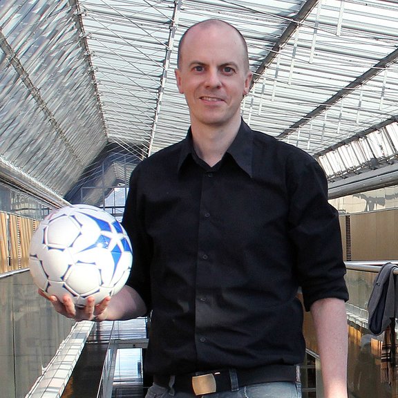 Hombre de pie en un edificio con un balón de fútbol bajo el brazo