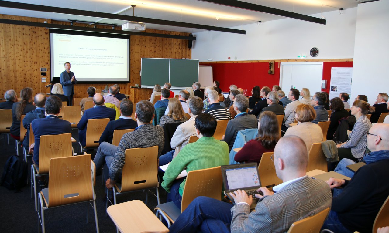 Viele Personen sitzen in einem Seminarraum und blicken auf eine Präsentation