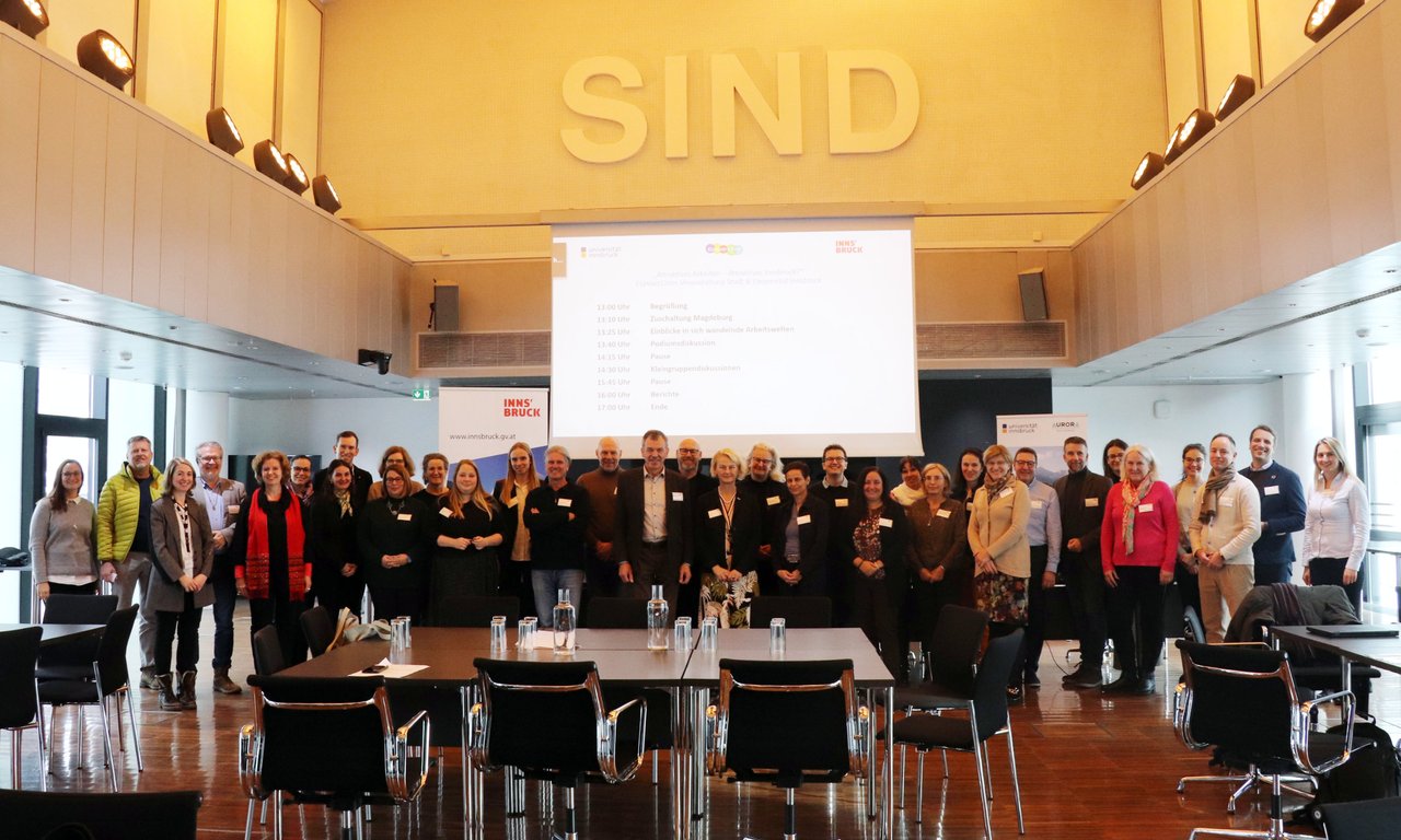Viele Personen in einem großen Saal stehen vor einer Leinwand, darüber der Schriftzug SIND