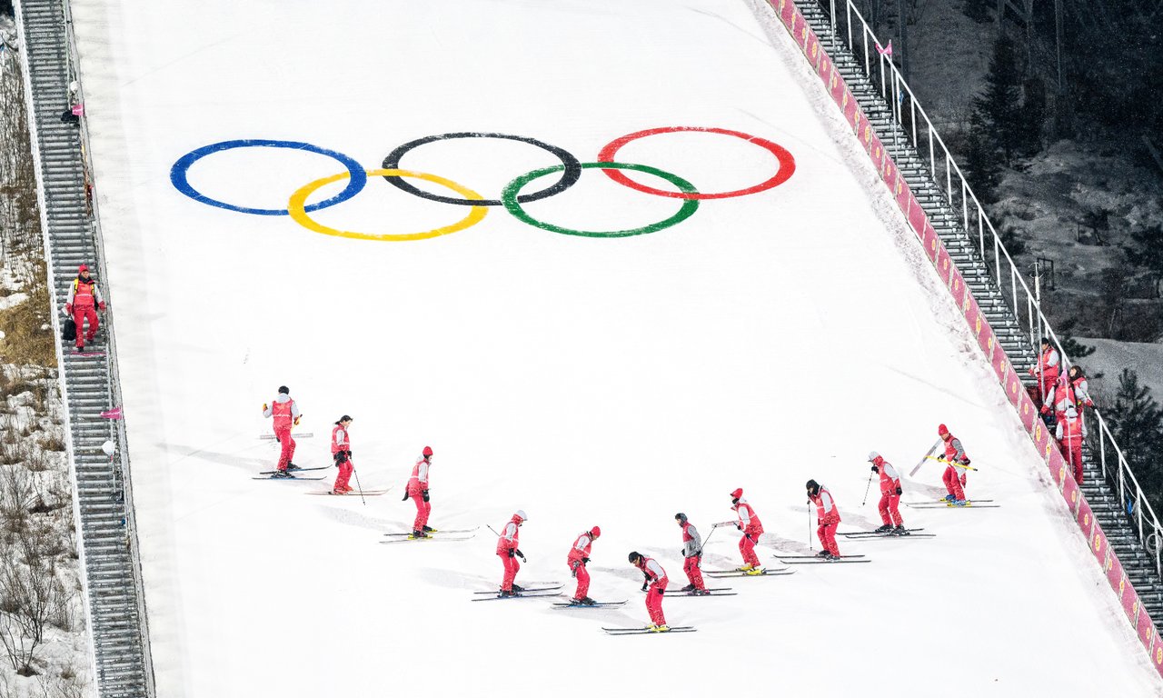 Auslauf einer Skisprungschanze mit den olympischen Ringen und zehn Skifahrern
