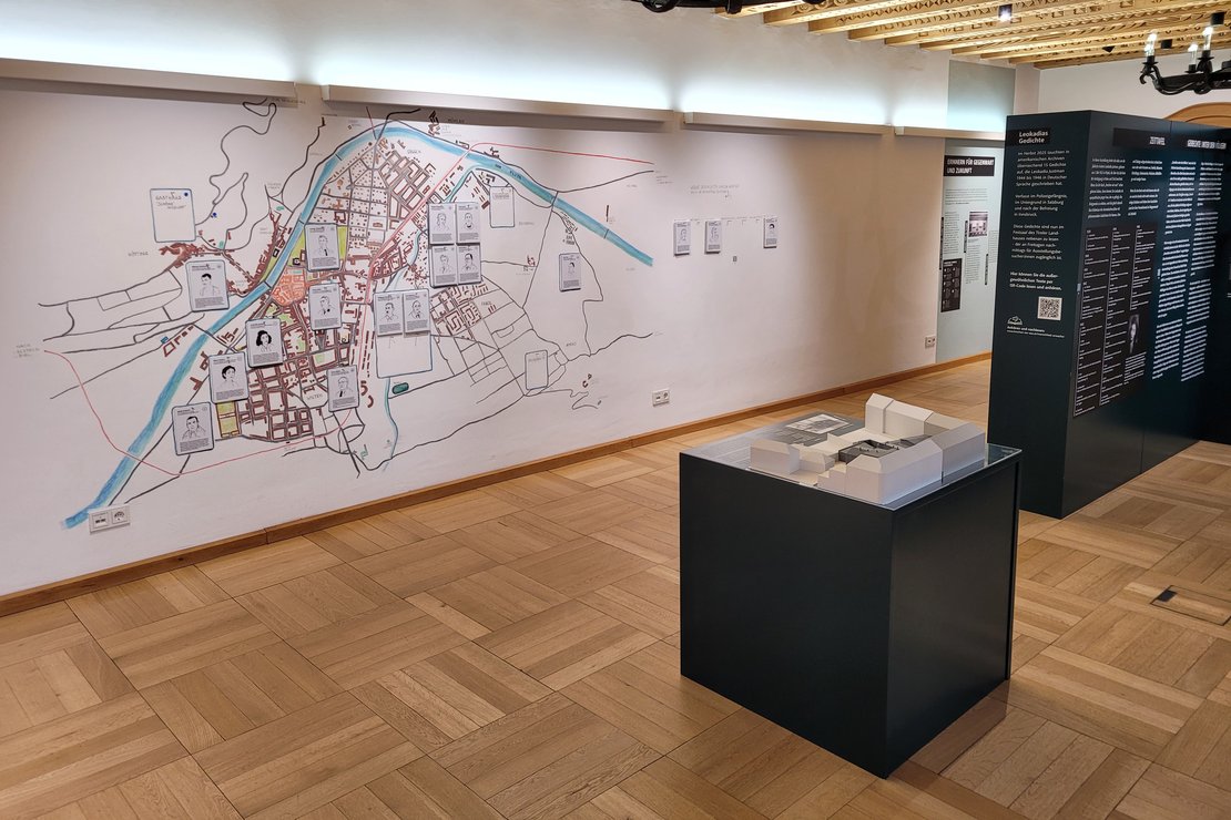 Blick in den Ausstellungsraum der Sonderausstellung "BRechen wir aus!" im Landhaus Tirol (Innsbruck). Zu sehen ist im Vordergrund ein Modell des Polizeigefängnisses, im Hintergrund eine Karte von Orten in Innsbruck, wo Leokadia wirkte.