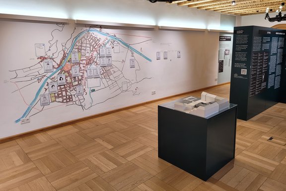 Blick in den Ausstellungsraum der Sonderausstellung "BRechen wir aus!" im Landhaus Tirol (Innsbruck). Zu sehen ist im Vordergrund ein Modell des Polizeigefängnisses, im Hintergrund eine Karte von Orten in Innsbruck, wo Leokadia wirkte.