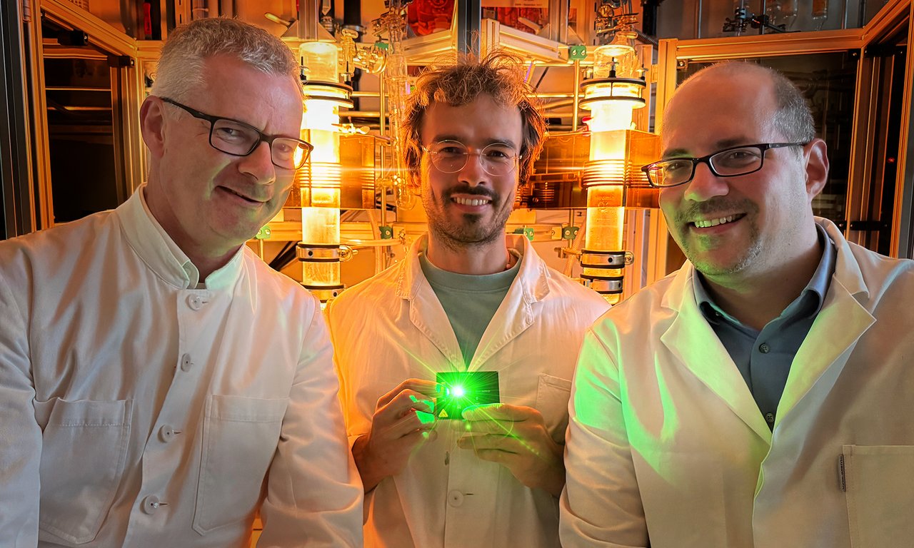Three people, one holding a green glowing instrument in the middle, glowing devices in the background