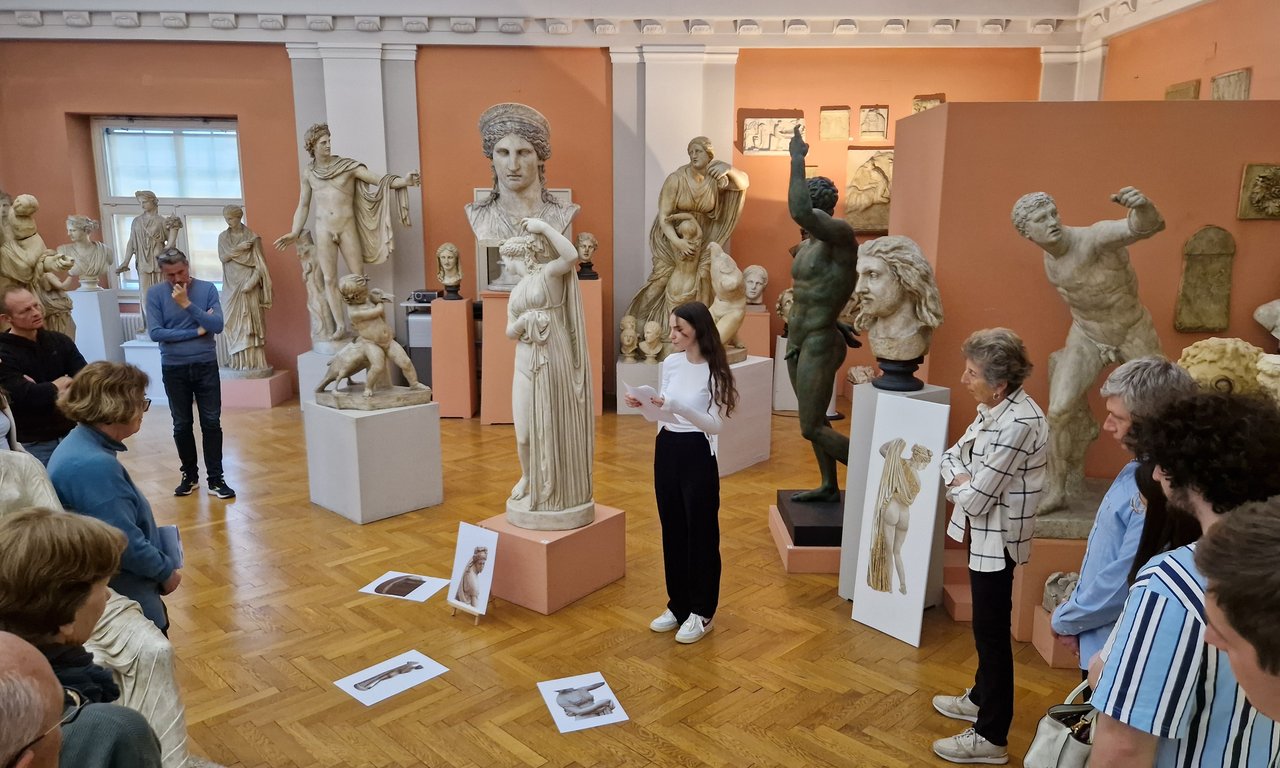 Blick in das archäologische Universitätsmuseum im Hauptgebäude, eine Frau präsentiert, Publikum steht um sie herum und hört zu.