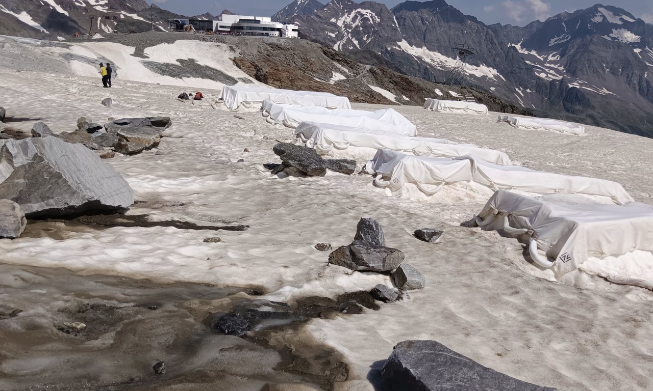 Ein Testfeld für die Gletscherforschung am Stubaier Gletscher. Mehrere rechteckige Flächen des Gletschers sind mit weißen Planen abgedeckt. Nach sechs Wochen Auslegung lässt sich der schützende Effekt der Planen bereits deutlich feststellen.