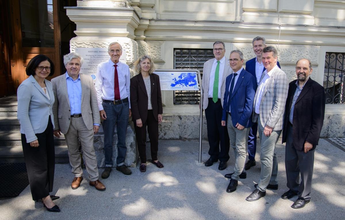 Mehrere Personen stehen vor einem Gebäude, in der Mitte eine Gedenktafel