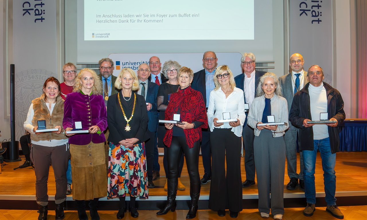 Zahlreiche Personen stehen auf einem Podium vor einer Leinwand