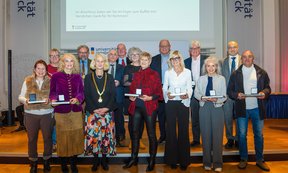 Zahlreiche Personen stehen auf einem Podium vor einer Leinwand