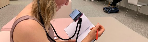 eine junge Frau nutzt die Handylesehilfe und schreibt gerade in ihrem Notizbuch