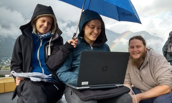 Drei Personen sitzen unter einem Schirm mit einem Laptop