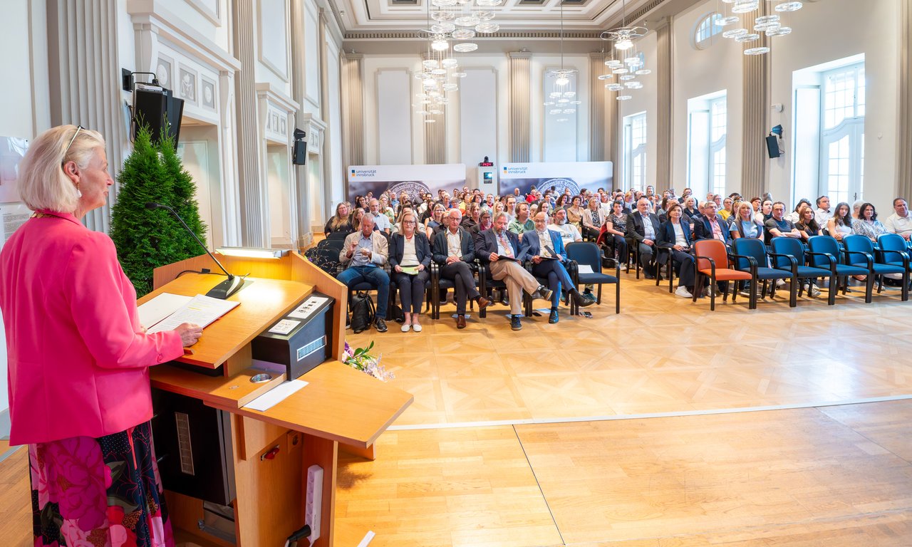 Rektorin der Universität Innsbruck spricht Grußworte vor einer voll besetzten Aula.