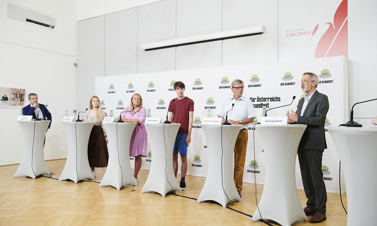 Sechs Personen an Stehtischen mit Mikrofonen präsentieren den Klimabericht