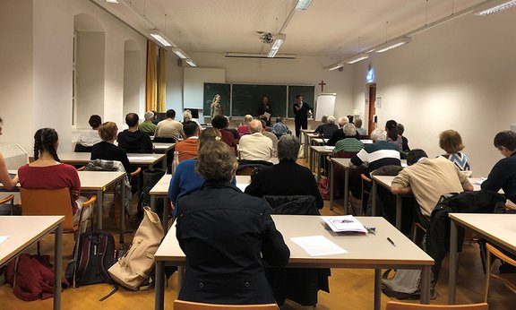 Personen sitzen im Seminarraum und hören Vortragenden zu