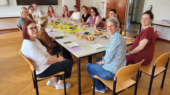 Zu sehen sind die Mitglieder des Instituts. Sie sitzen an einem gedeckten Tisch.