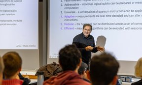 Jay Gambetta vor einer Leinwand, auf der Text zu lesen ist, im Vordergrund Publikum.