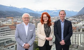 Drei Personen stehen auf einer Dachterasse, im Hintergrund ein Blick über Innsbruck