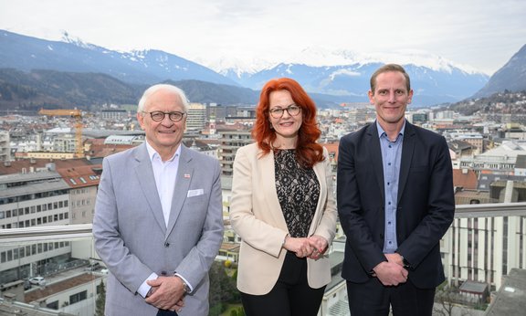 Drei Personen stehen auf einer Dachterasse, im Hintergrund ein Blick über Innsbruck