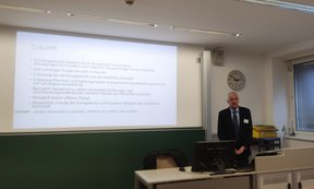 Zu sehen ist Wilhelm Rees in einem Hörsaal. Er hält einen Vortrag.