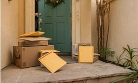 Pakete und Polsterkuverts liegen auf der Stufe vor einer Haustüre.