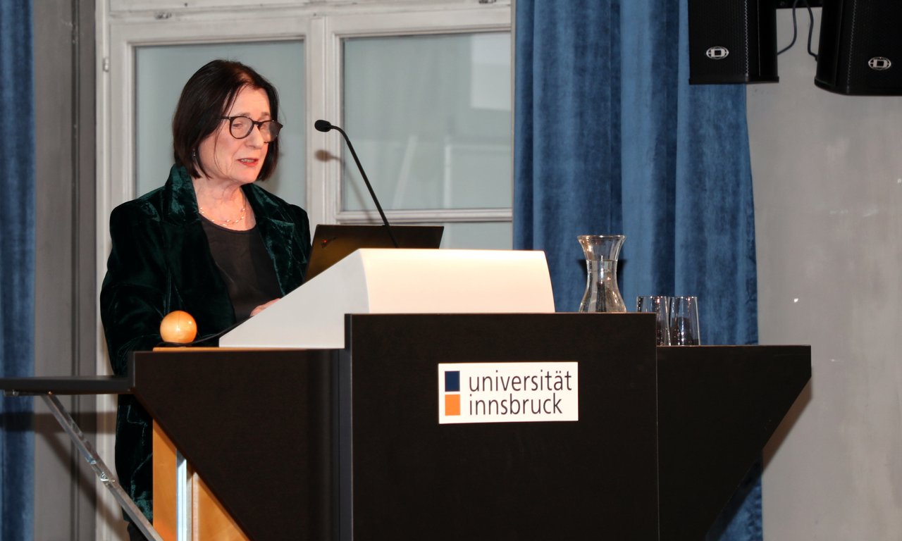 Irina Sherbakova steht an einem Rederpult und lies von einem Laptop ab.