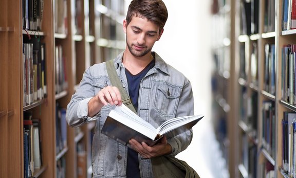Student in Bibliothek mit Buch in der Hand