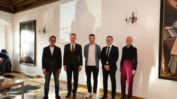 Three award winners (on the right) stand next to the VR Fügenschuh and Prof. Piater. The fourth winner is projected to the wall behind them.