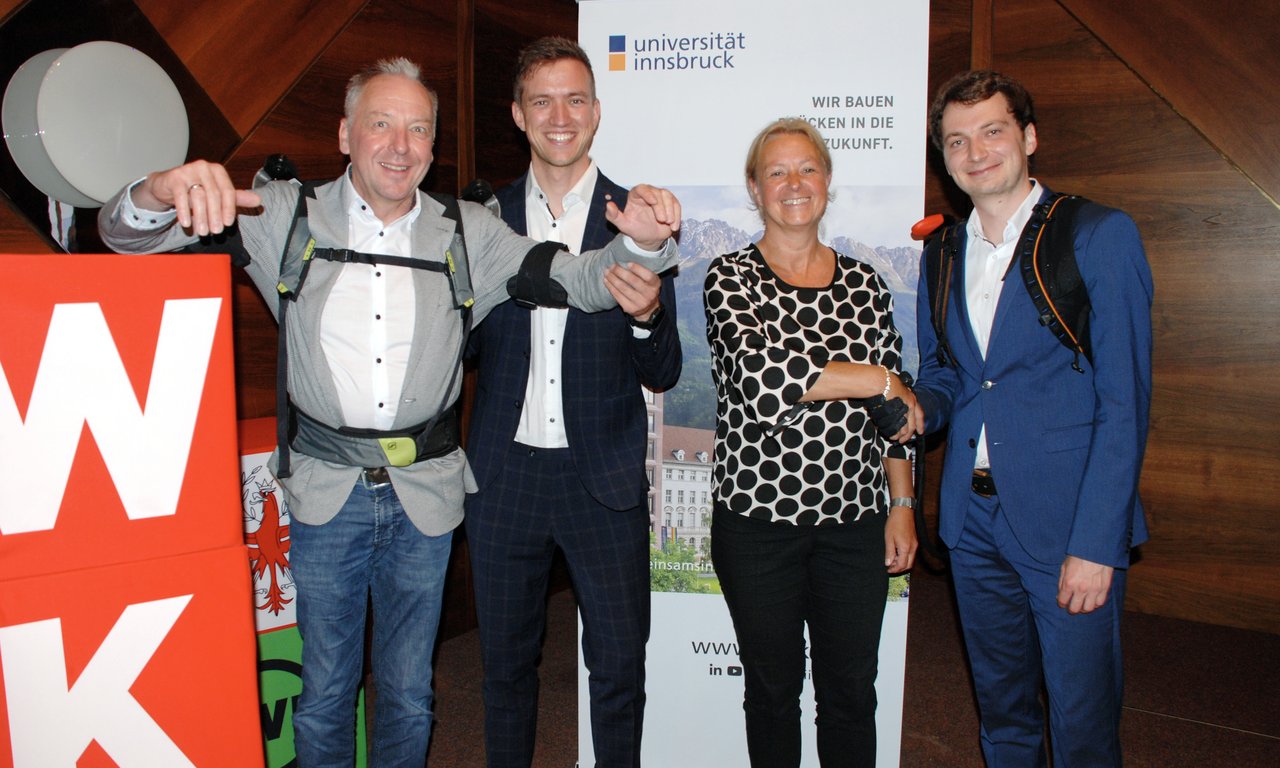 Vier Personen stehen vor einem Rollup. Die beiden Personen links und rechts tragen ein Exoskelett.
