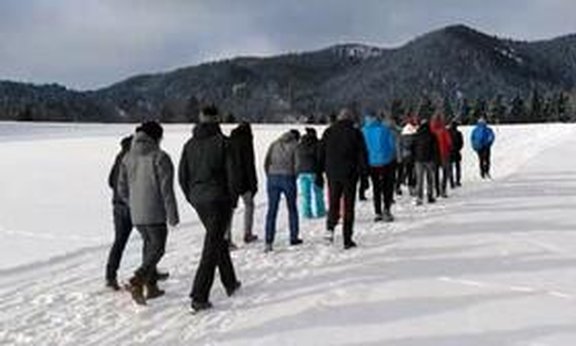 Mehrere Personen gehen in die selbe Richtung über ein schneebedecktes Feld.