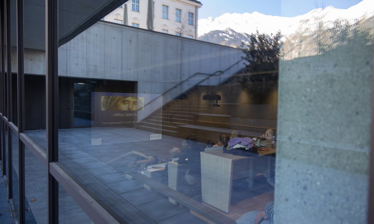 Foto durch die Scheibe des Agnes-Heller-Haus mit Blick auf die Folie einer Präsentation, auf der "Who Cares?" steht.