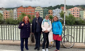 Vier Personen stehen am Innsbrucker Marktplatz für ein Gruppenfoto nebeneinander, hinter ihnen der Inn und Häuser der Mariahilfstraße.