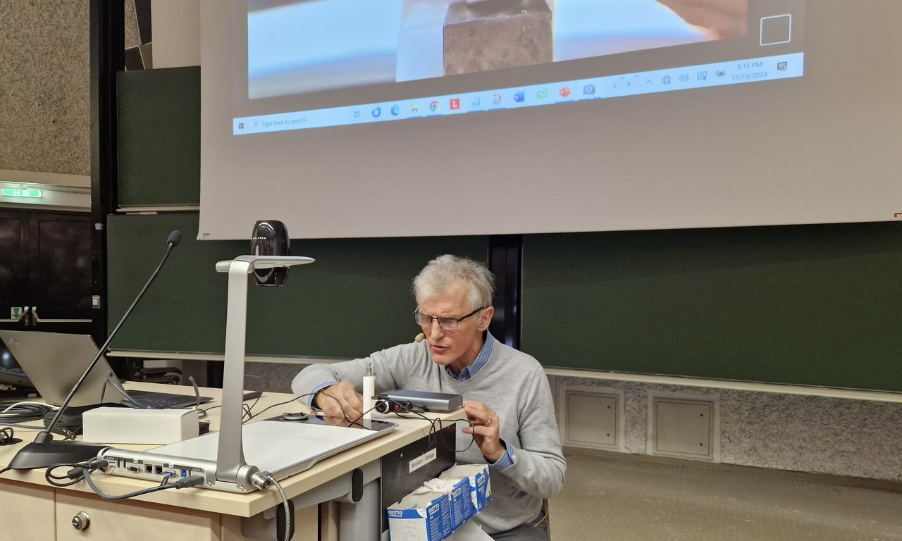 Ein Mann kniet im vorderen Bereich eines Hörsaals.