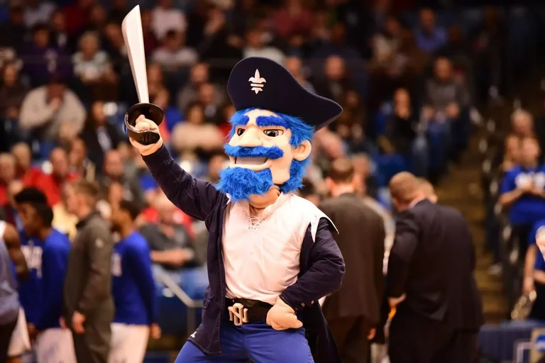 Ein US-Unimaskottchen, der Pirat Bruno steht mit hoch erhobenem Säbel vor einer jubelnden Menge. Haare und Bart sind blau, auf seinem Kopf trohnt ein Piratenhut.