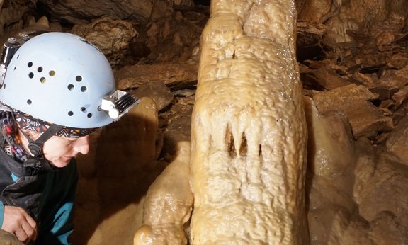 Höhlenforscher mit Helm kniet vor einem Stalagmiten.