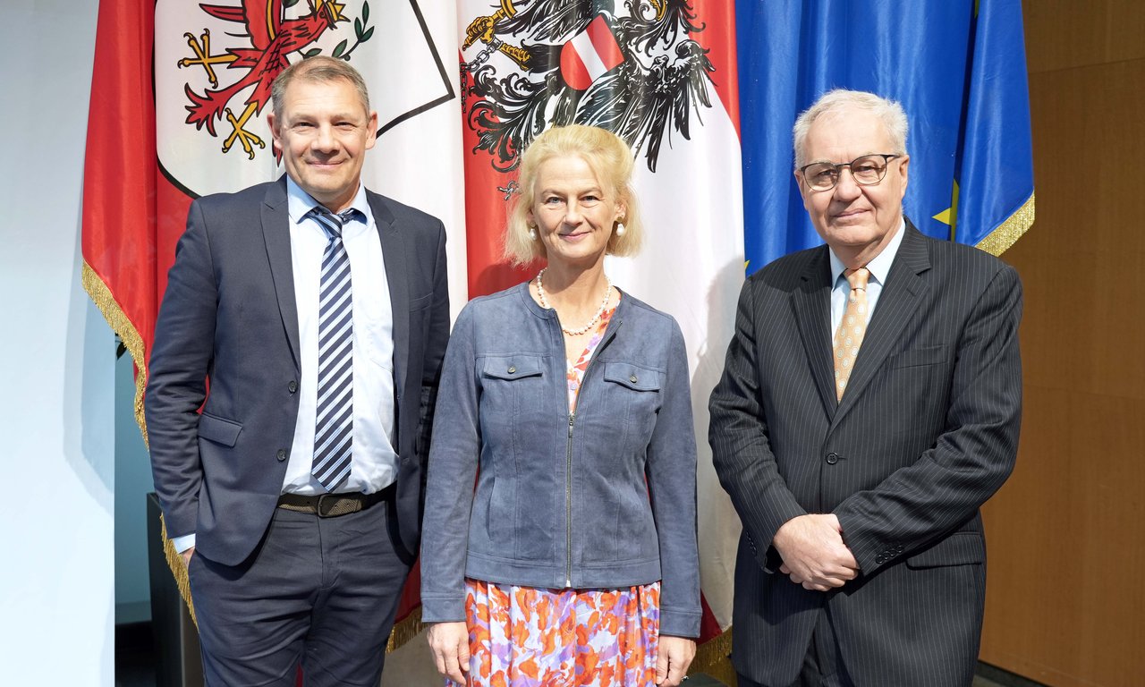 Drei Personen stehen neben einander vor drei Fahnen (Tirol, Österrreich, EU)