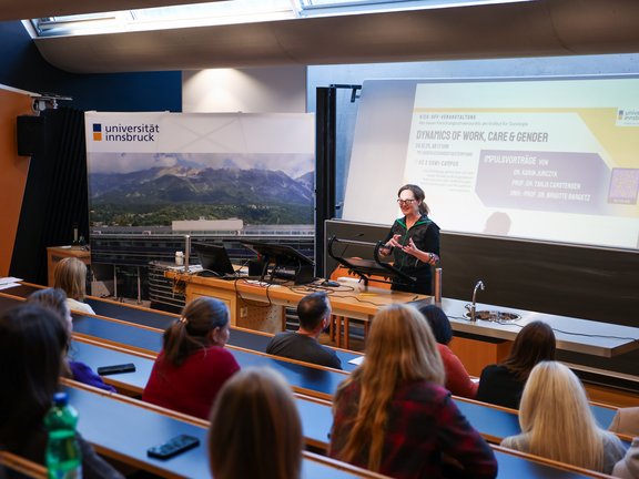Hörsaal, Zuhörende von hinten, Votragende vor einer Powerpoint-Präsentation