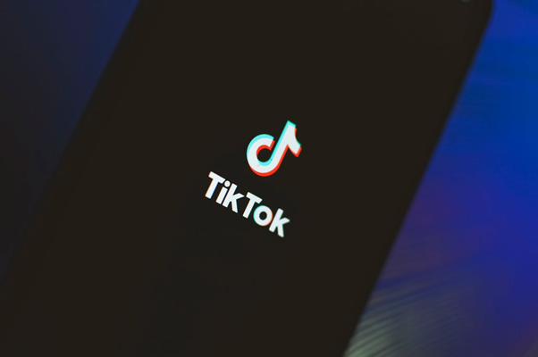 Das Bild zeigt das weiße TikTok-Logo, eine stilisierte Musiknote mit blauem und rotem Schatteneffekt, sowie den Schriftzug „TikTok“ auf dem dunklen Bildschirm eines Smartphones.