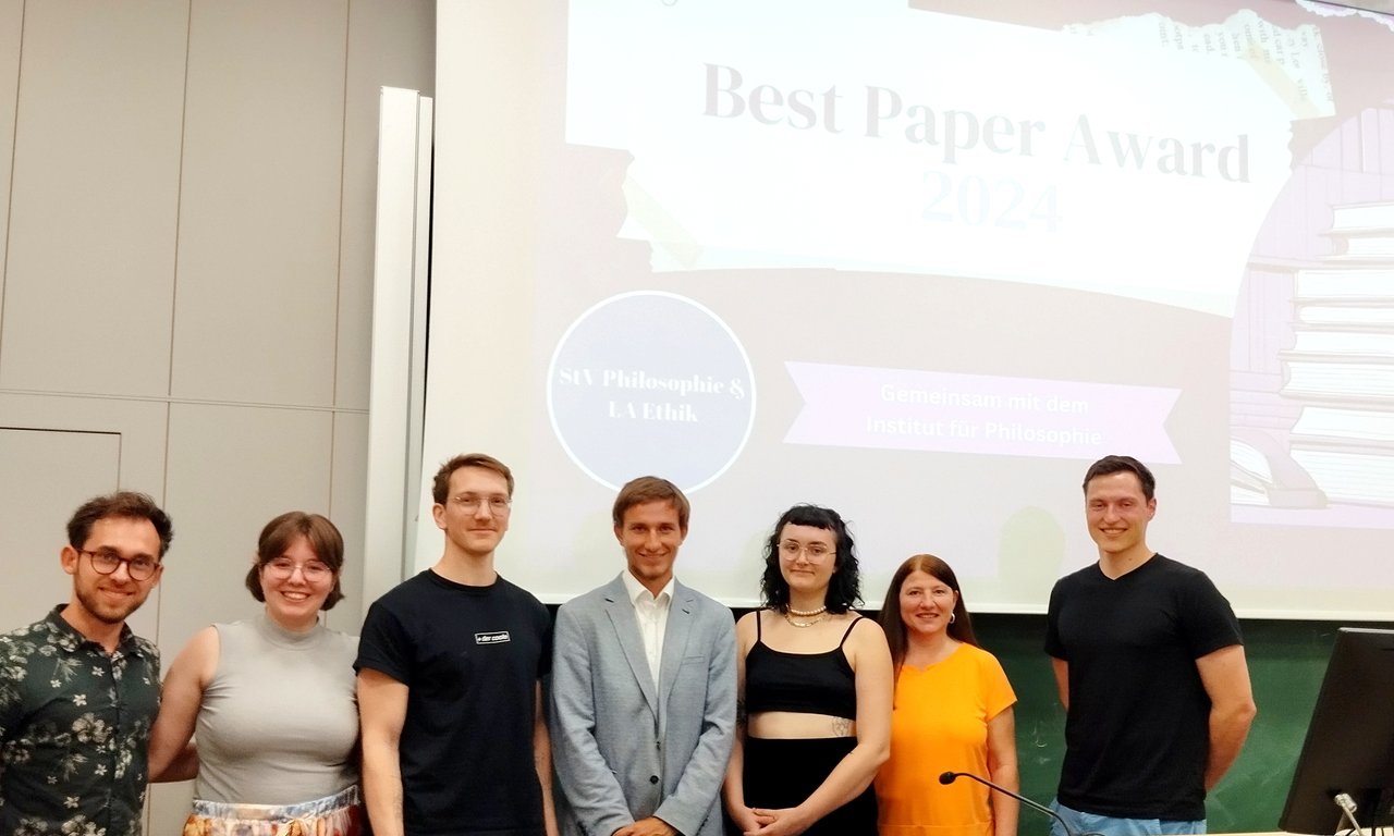 Gruppenfoto mit sieben Personen im vorderen Bereich eines Hörsaals.