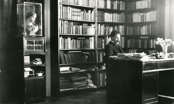 Schwarz-weiß-Foto: Ludwig von Ficker in seinem Arbeitszimmer in Mühlau um 1910, er sitzt vor einem großen Bücherregal an seinem Schreibtisch